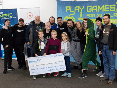 Group of smiling adults and kids crowded around a large cheque.