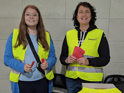 Two people wearing yellow safety vests and holding raffle tickets.