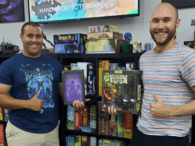 Two people giving the thumbs up holding board games.