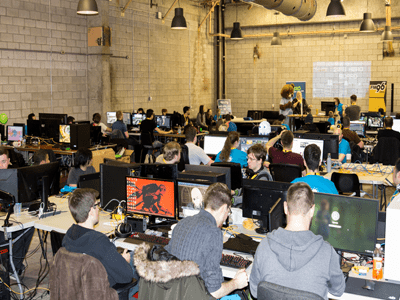 Room full of people sitting at desks with monitors playing video games.