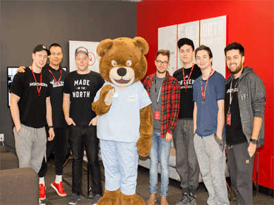 Group of LAN Party participants crowded around bear mascot smiling.