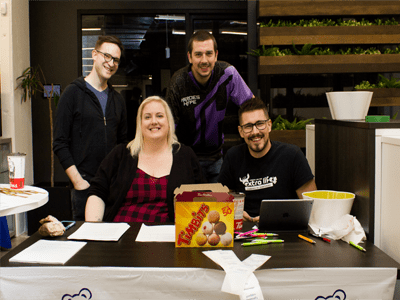 Four people smiling at the camera while sitting behind a registration table.