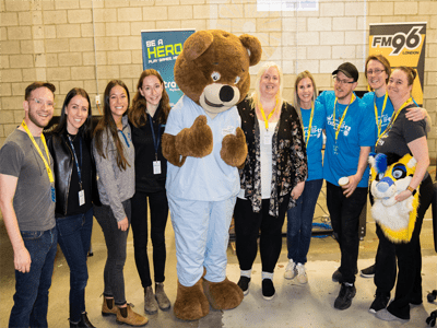 Group of people crowded around bear mascot smiling at the camera.