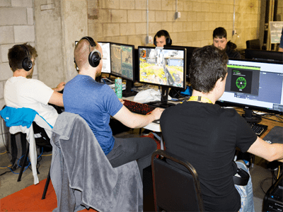 Row of gamers playing different video games at desks.